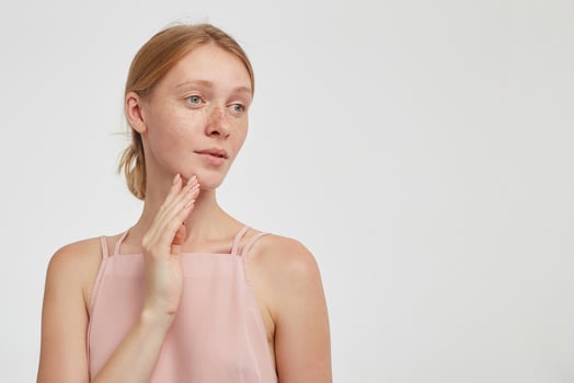 Portrait of young lovely redhead female with natural makeup raising hand to her face and looking meditatively aside while standing over white background photo