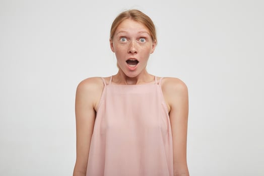 Astonieshed young pretty redhead female rounding her green eyes while looking amazedly at camera with wide mouth opened, isolated over white background photo