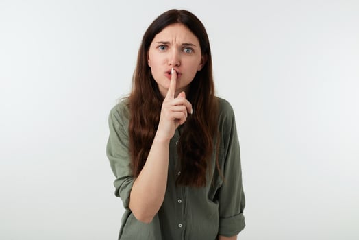 Severe young brunette woman with casual hairstyle frowning her eyebrows while looking seriously at camera and raising hand in hush gesture, isolated over white background photo