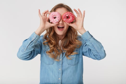 Young cool male wearing a denim shirt, with long blond wavy hair, looking through donuts and smiling broadly, isolated over white background. photo