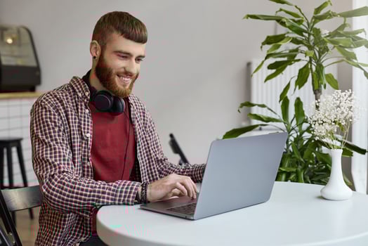 Happy young attractive ginger bearded man working at a laptop while sitting in a cafe, wearing in basic clothes, broadly smiling and enjoy the work. photo