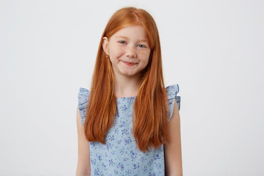 Portrait of petite cute calm smiling freckles red-haired girl wears in blue dress, stands over white background. photo