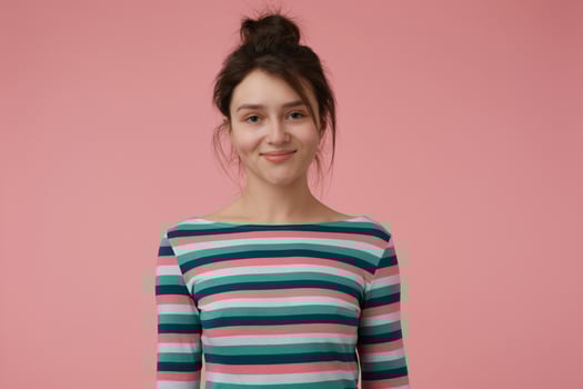 Young lady, pretty brunette woman with bun. Wearing striped blouse and have cute smile, happy to see you, showing confidence. Watching at the camera isolated over pastel pink background photo