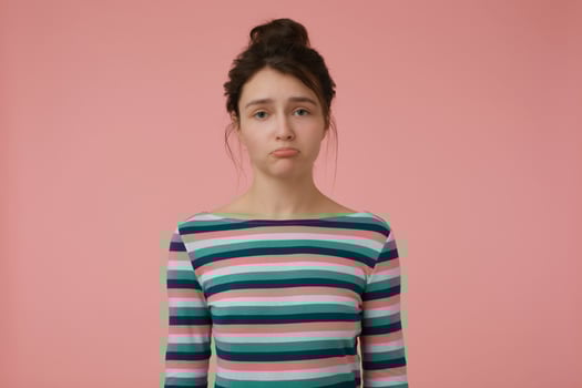 Young lady, unhappy woman with brunette hair and bun. Wearing striped blouse and pout a lip, offended. Emotional concept. Watching at the camera isolated over pastel pink background photo