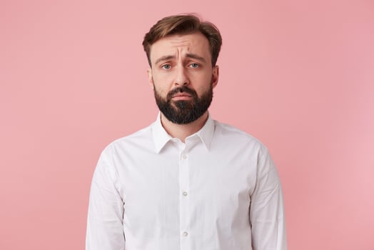 The handsome bearded man frowns and looks sadly at the camera, he was told the news unpleasant. Isolated over pink background. photo