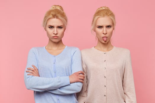 Frowning beautiful young blonde twins in a bad mood, looking in the camera isolated over pink background. photo