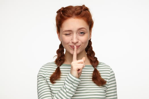 ginger young female smiling, wink and shows silence gesture photo