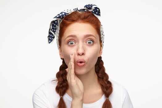 portrait of young ginger female standing over white studio background looks aside with shocked facial expression and whisper a secret photo