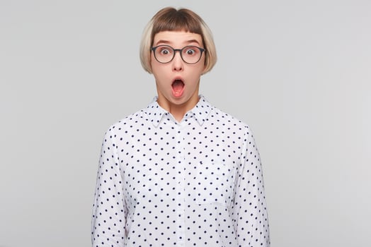 Portrait of amazed astonished blonde young woman with opened mouth wears polka dot shirt and glasses looks shocked and shouting isolated over white background photo