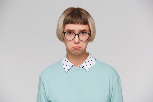 Closeup of sad upset young woman wears blue sweatshirt and spectacles feels depressed and looks unhappy isolated over white background photo