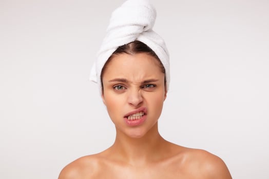 Studio photo of beautiful young brunette female without makeup twisting her mouth and grimacing face while posing over white background after shower