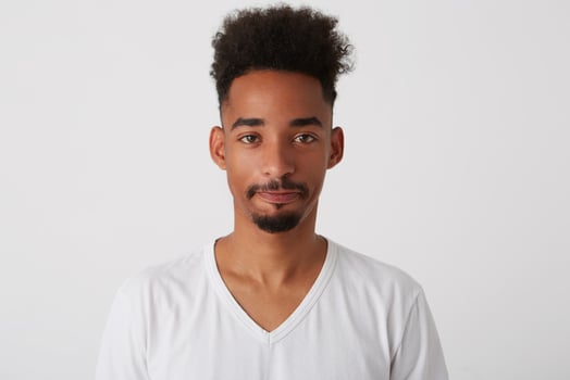 Portrait of young brown-eyed brunette man with dark skin keeping his lips folded while looking boringly at camera, isolated over white background in casual clothes photo