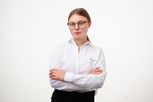 Indoor shot of young white-headed woman in glasses keeping her hands crossed on chest while looking calmly at camera, posing over white background in formal clothes photo