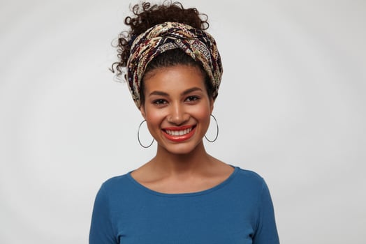 Portrait of young dark haired curly brunette lady with casual hairstyle showing her white perfect teeth while smiling cheerfully at camera, standing over white background photo