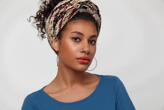 Portrait of pensive young attractive curly brunette woman with nose piercing looking attentively at camera and keeping lips folded, standing over white background photo