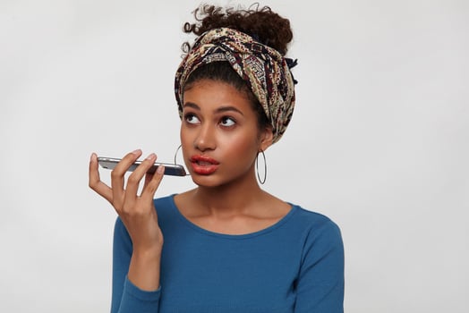 Puzzled young brown-eyed curly brunette female keeping smartphone in raised hand while having phone talk and looking upwards, isolated over white background photo