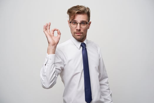 Attractive male with fashioned hairstyle, satisfied expression, shows okay sign, feels glad after work meeting, isolated over white background. Human facial expressions, body language photo