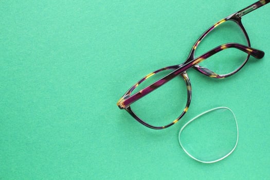 Old broken eyeglasses with damaged lens on green background. Poor eyesight. Reuse and repair concept. Idea of health. Failure optic eyewear. Breakage of vision correction glasses. Close up, flat lay photo