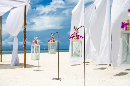 Beautiful wedding setting up on beach. White decoration with orchid flowers and candles over white sand. Idyllic romantic destination wedding or honeymoon, outdoor celebration. Beach wedding concept photo