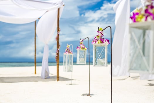Beautiful wedding setting up on beach. White decoration with orchid flowers and candles over white sand. Idyllic romantic destination wedding or honeymoon, outdoor celebration. Beach wedding concept photo