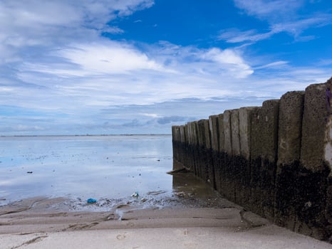 a large rock blocking the waves surrounded by small shells, and also a view of the sea with some plastic rubbish on the beach photo