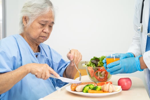 Asian senior woman patient eating Salmon steak breakfast with vegetable healthy food while sitting and hungry on bed in hospital. photo