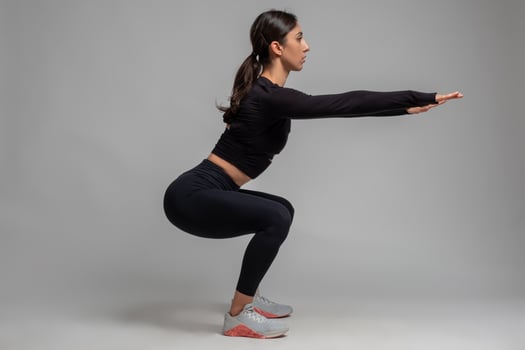Side view of girl doing squats on grey background photo