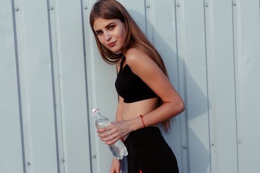 Female athlete drinking water while standing by a grey wall. photo