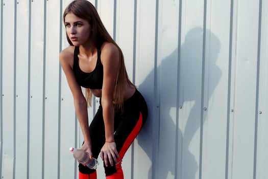Female athlete drinking water while standing by a grey wall. photo