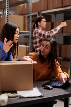 Warehouse operator supervising coworker doing inventory on laptop in storage room. Storehouse young asian women employees discussing goods logistics and distribution schedule photo
