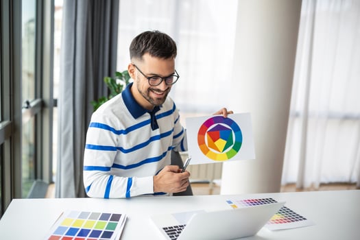 Young Freelance Graphic Designer Guy Working With Laptop And Color Swatches, Sitting At Desk In Home Office, Choosing Colour Gamma For New Design Project, Side View With Copy Space photo