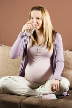 Pregnant woman sitting on the sofa and drinking water photo
