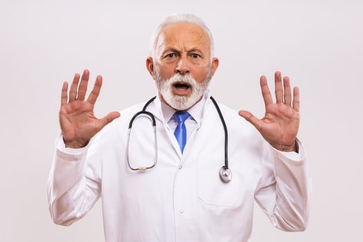 Portrait of  senior doctor in panic on gray background. photo