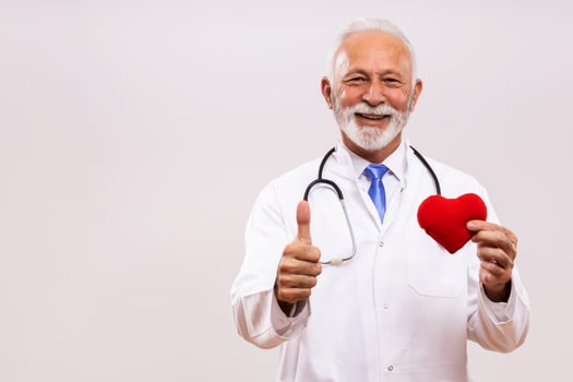 Portrait of senior doctor with stethoscope showing heart shape and thumb up on gray background. photo