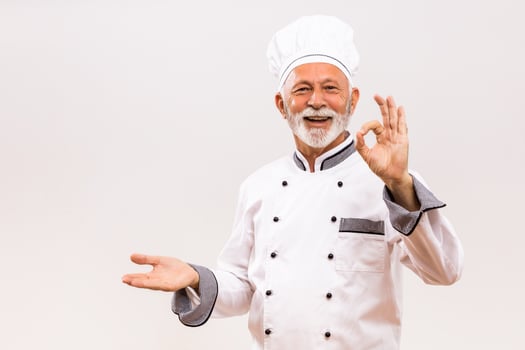 Portrait of senior chef showing palm of hand and ok sign on gray background. photo