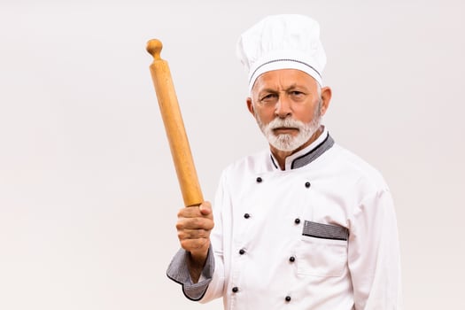 Image of angry senior chef holding rolling pin on gray background. photo