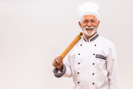 Portrait of senior chef with rolling pin on gray background. photo