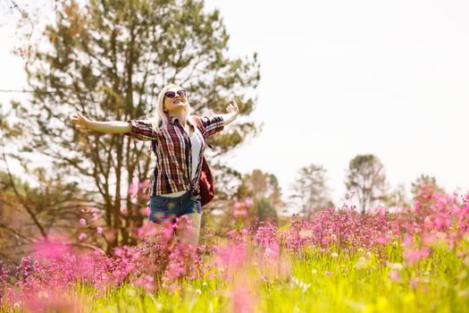 Happy adventurer female stands on the green mountain slope among flowering pink rhododendrons and looking into the distance. Epic travel in the mountains. Wide angle. photo