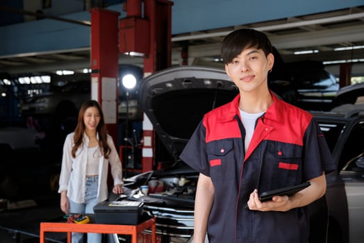 Portrait of young Asian male automotive mechanic worker with female customer's EV car at maintenance garage, happy smiles, professional service station, check and repair in auto transport industry. photo