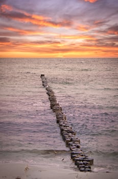 Groynes jut out into the Baltic Sea. Sunset on the horizon. Wooden logs protecting photo