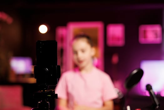 Close up shot of professional recording cellphone camera used by young internet star to do livestream. Focus on video production gear used by child in blurry background to do live broadcast photo