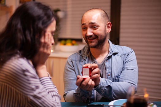 Young man asking wife to marry him during dinner in kitchen. Man making proposal to his girlfriend in the kitchen during romantic dinner. Happy caucasian woman smiling being speechless photo