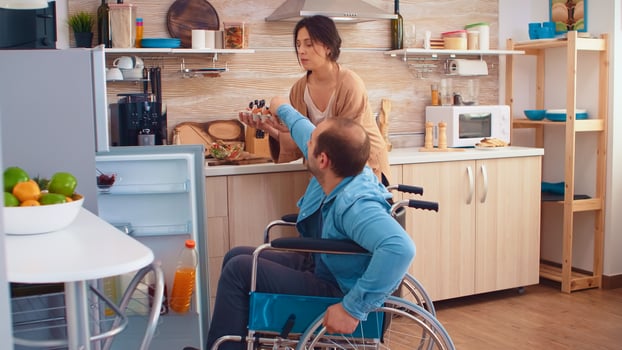Disabled man in wheelchair helping wife in kitchen. Opening refrigerator. Guy with paralysis handicap disability handicapped difficulties getting help for mobility from love and relationship photo