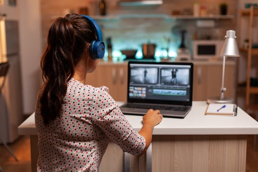 Video editor working on a project from home kitchen during night time and listening music on headphones. Content creator in home working on montage of film using modern software for editing. photo