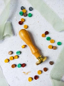 a top view of colorful wax bead and sealing wax with green silk ribbon on an old grey surface photo
