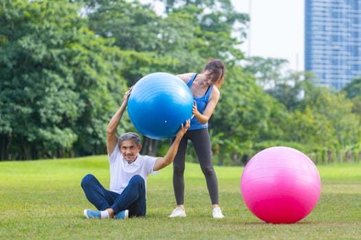 Senior asian man and his supporting daughter are exercising with yoga ball in public park to build core body muscle for elder longevity exercise and outdoor workout photo