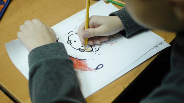 High angle view of boy drawing with color pencil on paper at desk in classroom. Clip. A cute little boy drawing with a pencil close up photo