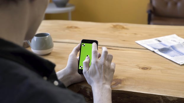 One guy holding in arms electronics gadget with green screen chromakey, scrolling and tapping it on wooden table background. Stock footage. Human sit and use the handheld cellphone in room. photo