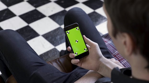 Male holding black smart phone with green screen and tracking marks on black and white checkered floor background. Stock footage. Man using and watching at mobile phone with chroma key. photo