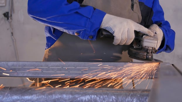 Craftsman sawing metal with disk grinder in workshop. Grinding metal with sparks flying. Electric wheel grinding on steel structure in factory Low speed shutter. Metal grinding with orange flying photo